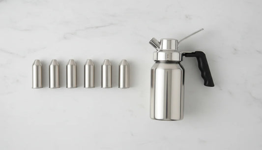 Multiple N2O whipped cream dispenser cartridges lined up beside a stainless steel dispenser